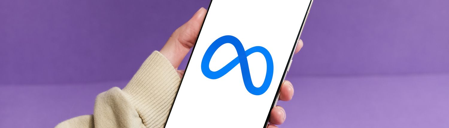 purple background with arm and hand in view holding a smart phone with the Meta logo on the screen