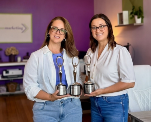 Dunn Marketing leadership including CEO & Brand Strategist Laura Dunn (left) and VP Client Services Marci Seney (right) holding the agency's 3 Communicator Award statues for 2026 at their Danielson office