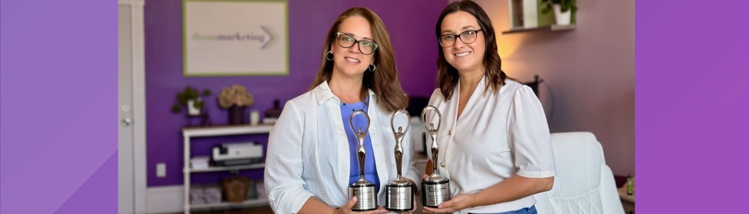banner_2026-07 communicator award Dunn Marketing leadership including CEO & Brand Strategist Laura Dunn (left) and VP Client Services Marci Seney (right) holding the agency's 3 Communicator Award statues for 2026 at their Danielson office