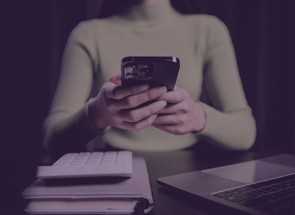 a woman holding a smart phone sitting at a black table with a laptop open