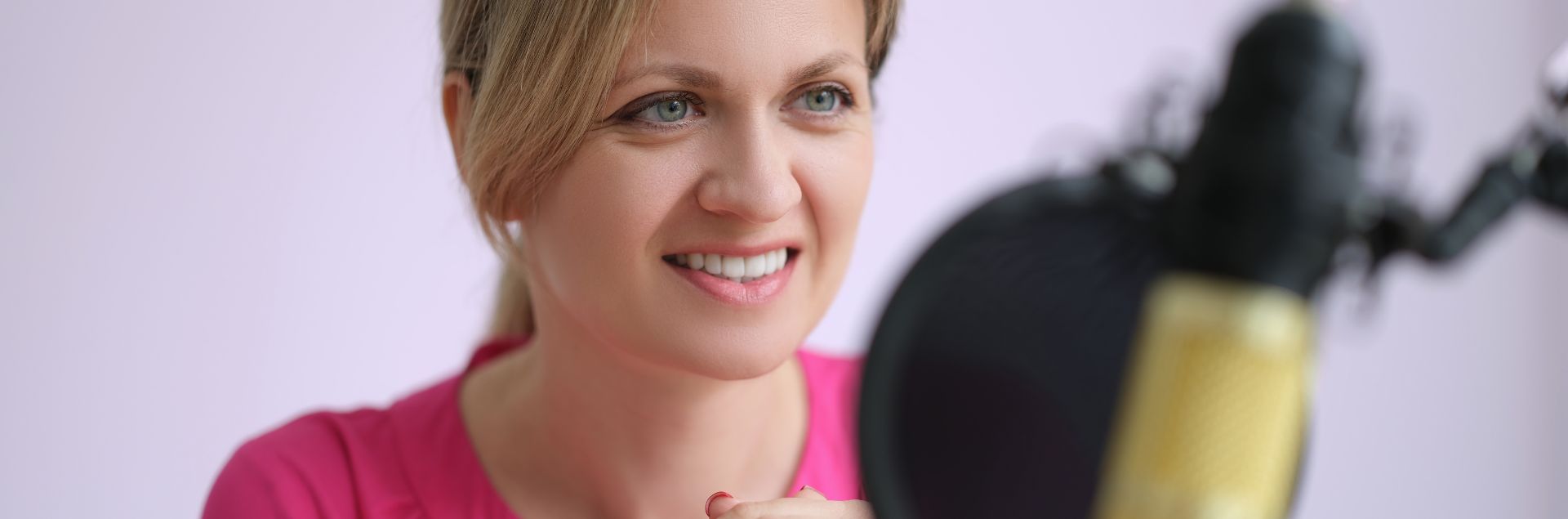 a woman smiling as she sits in front of a microphone in a recording studio