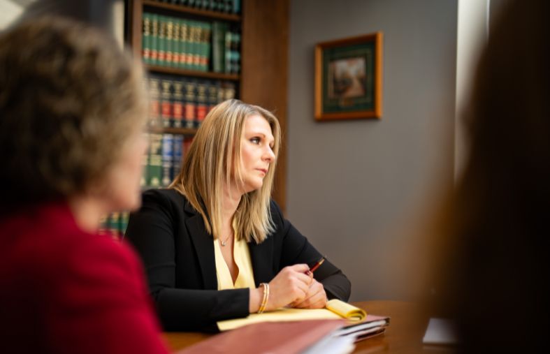 a lawyer sits at a conference table with her paralegal team in front of a bookcase full of legal books